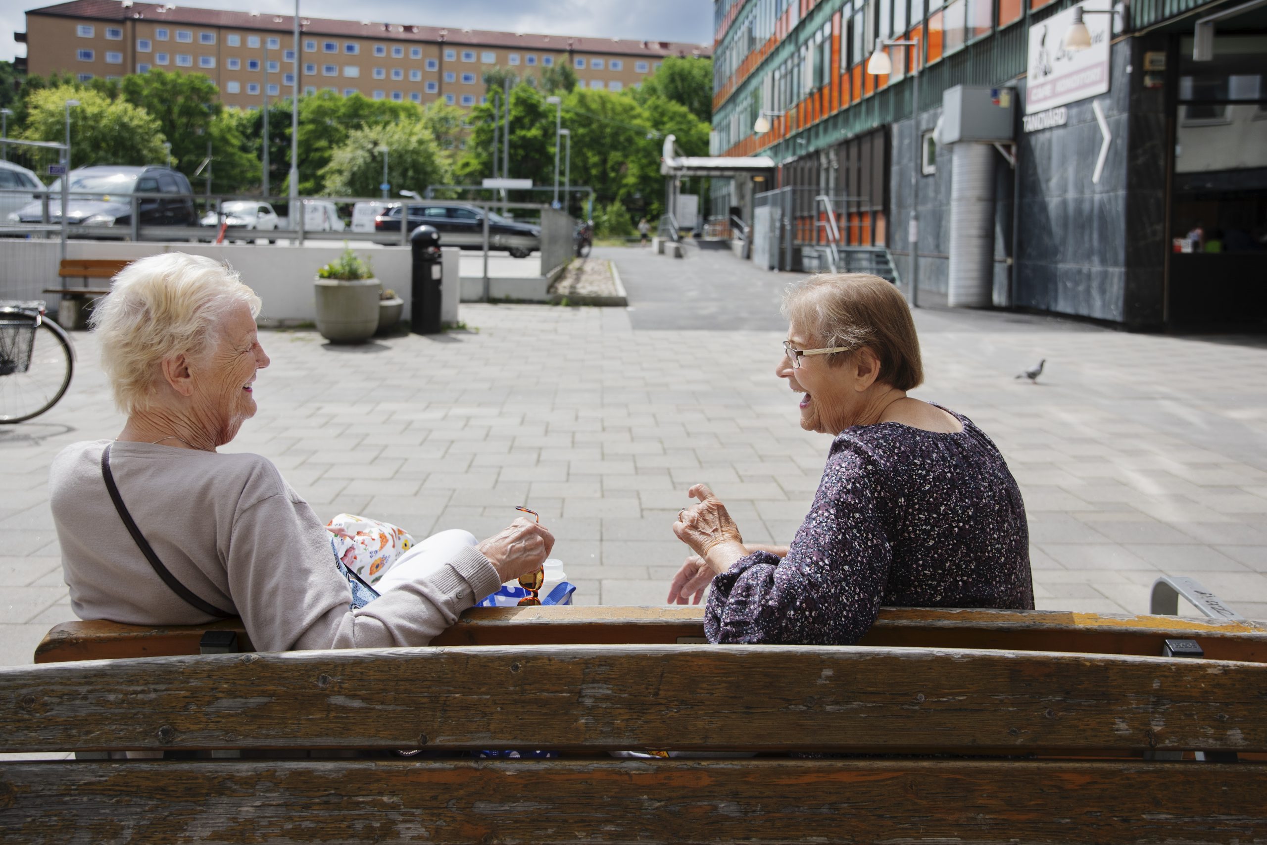 Två personer sitter på en bänk i solen och samtalar och skrattar.